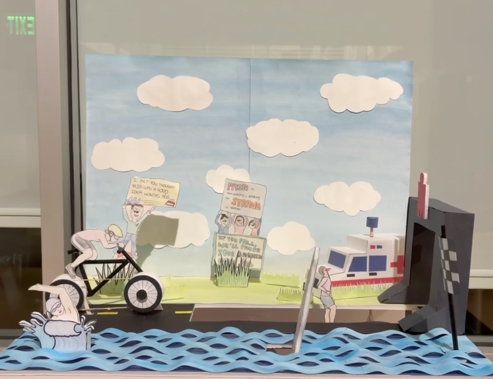 Hand-crank automaton with an illustrated scene, a bicycle, figures, and layered blue waves.