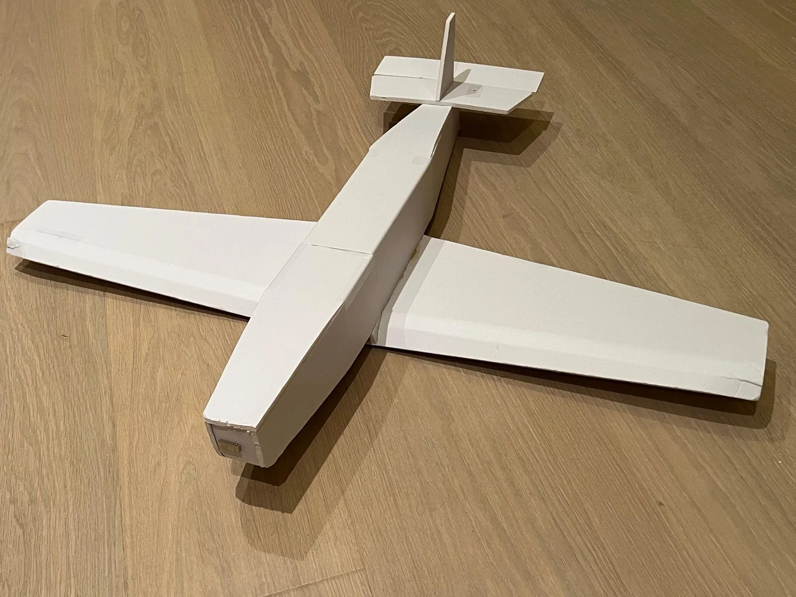 First glider aircraft build, with a white fuselage, broad wing, and tail assembly on a wooden floor.